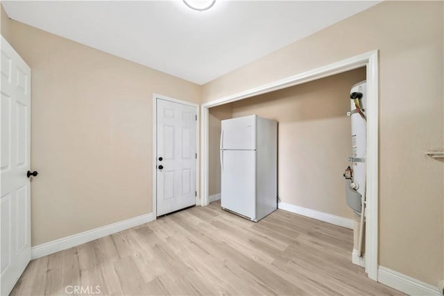 unfurnished bedroom featuring freestanding refrigerator, light wood finished floors, and baseboards