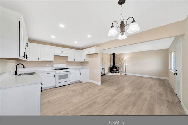 kitchen featuring white gas stove, a sink, light countertops, a wood stove, and a chandelier