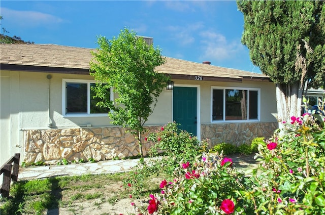 property entrance featuring stone siding, stucco siding, and a shingled roof