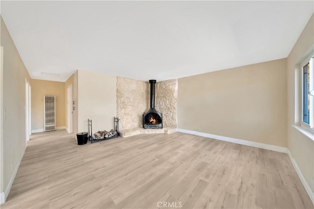unfurnished living room featuring light wood-style flooring, baseboards, a heating unit, and a wood stove