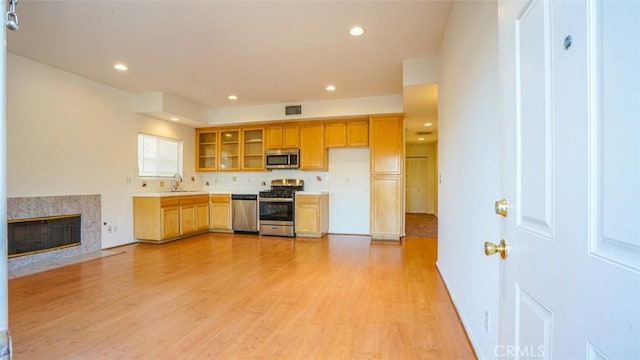 kitchen featuring sink, light hardwood / wood-style flooring, a high end fireplace, and stainless steel appliances