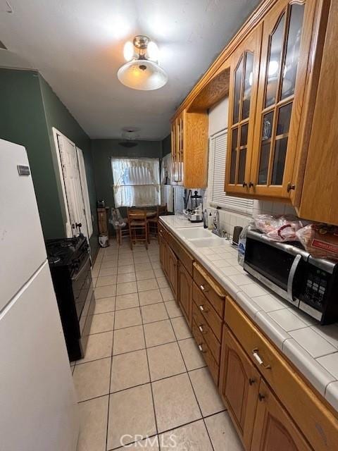 kitchen with sink, black range with gas stovetop, light tile patterned floors, tile countertops, and white fridge