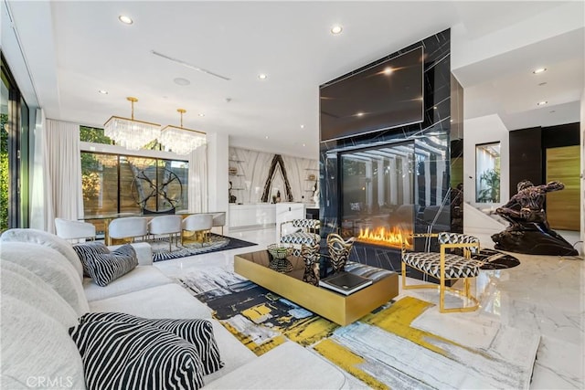 living room featuring a glass covered fireplace, recessed lighting, marble finish floor, and a chandelier