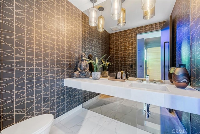 bathroom with marble finish floor, tile walls, toilet, and a sink