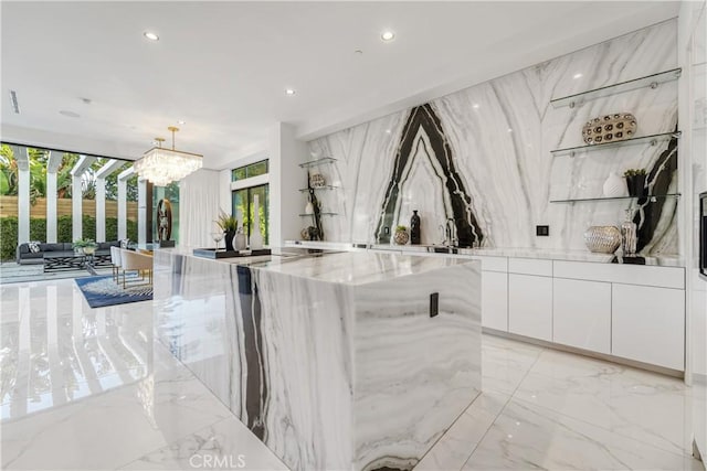 interior space featuring a notable chandelier, light stone countertops, white cabinetry, decorative light fixtures, and expansive windows