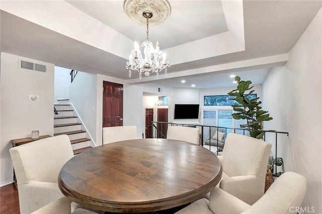 dining space with hardwood / wood-style floors, a raised ceiling, and a chandelier