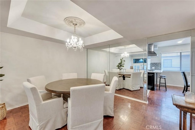 dining area with parquet flooring, a raised ceiling, and an inviting chandelier