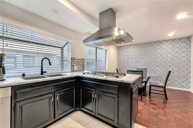 kitchen featuring light stone countertops, sink, kitchen peninsula, island range hood, and stainless steel gas cooktop