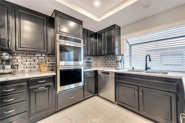 kitchen featuring stainless steel appliances, decorative backsplash, sink, light stone counters, and a tray ceiling