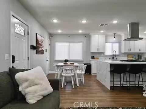 kitchen with a kitchen bar, white cabinetry, range hood, a kitchen island, and dark wood-type flooring