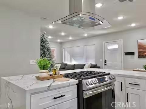 kitchen featuring light stone counters, white cabinets, stainless steel gas range, and island range hood