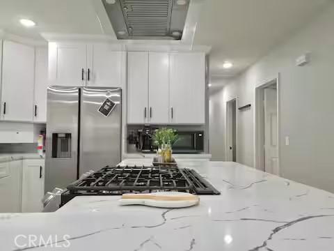 kitchen with white cabinets, ventilation hood, stainless steel fridge, and light stone counters