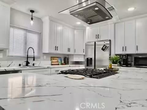 kitchen with pendant lighting, white cabinetry, stainless steel fridge, light stone counters, and range hood