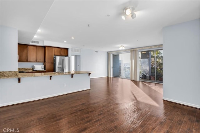 kitchen with kitchen peninsula, a breakfast bar, stainless steel appliances, light stone counters, and dark hardwood / wood-style floors