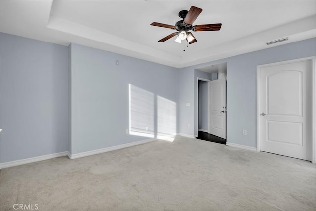 carpeted spare room with ceiling fan and a tray ceiling