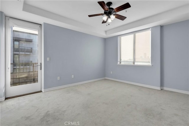 carpeted empty room featuring ceiling fan and a raised ceiling