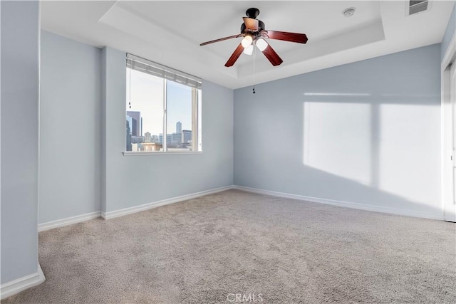 carpeted empty room featuring ceiling fan and a raised ceiling