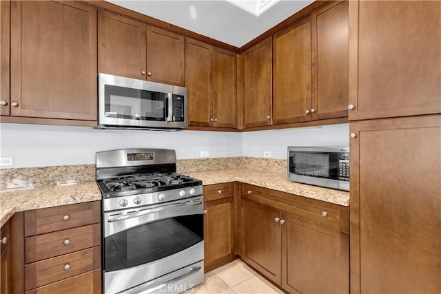 kitchen with stainless steel appliances, light stone counters, and light tile patterned flooring