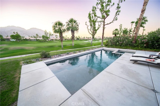 pool at dusk featuring a lawn, a mountain view, and a patio area