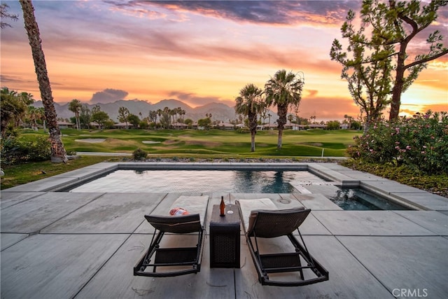 pool at dusk featuring a mountain view, a patio area, a lawn, and a jacuzzi