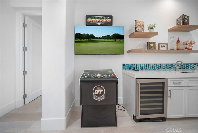 interior space featuring decorative backsplash, white cabinets, beverage cooler, and sink