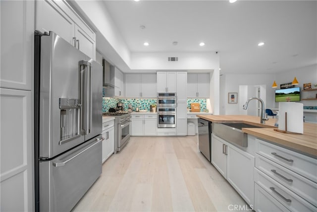 kitchen with wooden counters, sink, white cabinets, decorative backsplash, and high end appliances