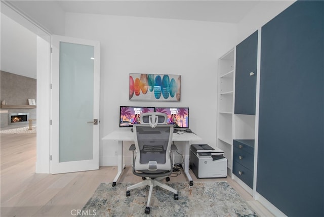 home office with a large fireplace and light hardwood / wood-style flooring