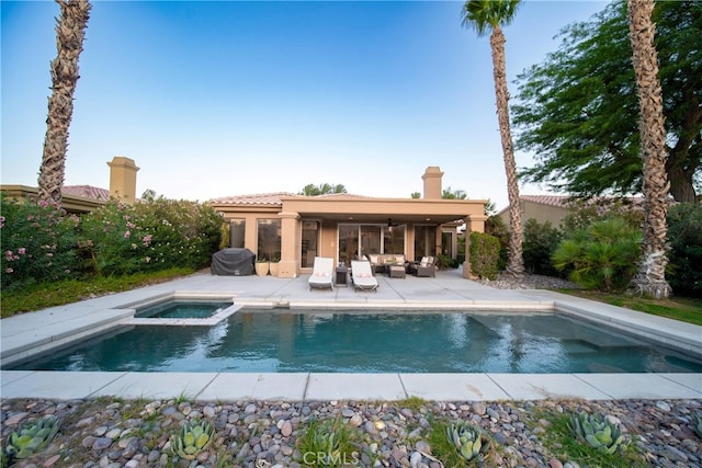 rear view of property featuring a pool with hot tub, a patio area, and outdoor lounge area