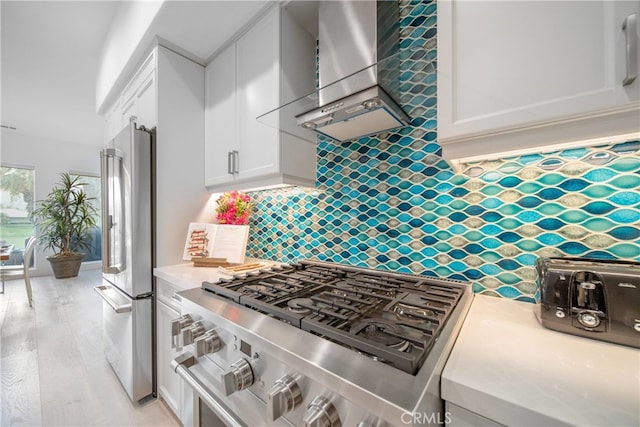 kitchen featuring light hardwood / wood-style floors, appliances with stainless steel finishes, decorative backsplash, wall chimney range hood, and white cabinets