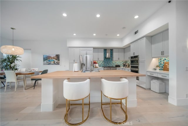 kitchen with butcher block counters, stainless steel appliances, an island with sink, decorative backsplash, and hanging light fixtures