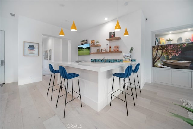 kitchen with kitchen peninsula, a kitchen bar, pendant lighting, and light hardwood / wood-style flooring