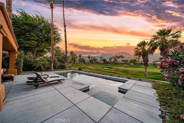 pool at dusk with a lawn, a mountain view, and a patio area