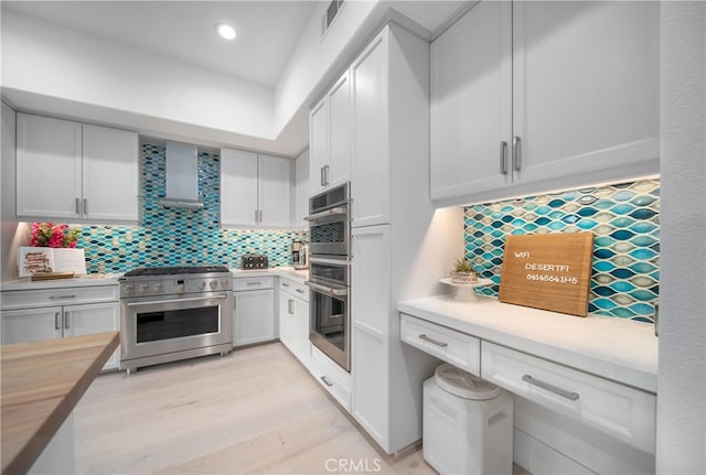 kitchen featuring tasteful backsplash, white cabinetry, wooden counters, wall chimney exhaust hood, and stainless steel range