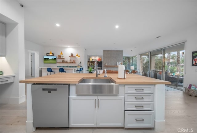 kitchen with white cabinetry, stainless steel dishwasher, sink, a center island with sink, and butcher block countertops