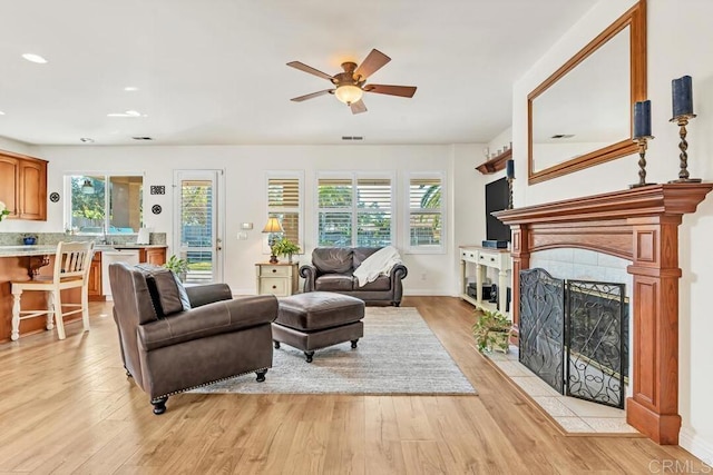 living room featuring a fireplace, ceiling fan, and light wood-type flooring