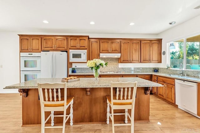 kitchen with light stone counters, a kitchen bar, white appliances, and a kitchen island