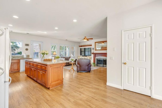 kitchen with light wood-type flooring, a center island, ceiling fan, light stone counters, and white appliances