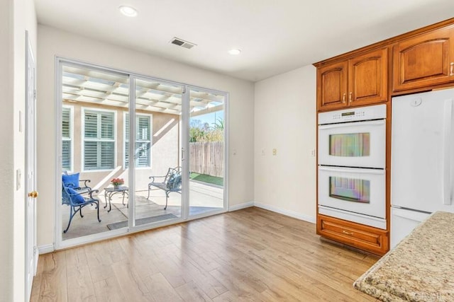 kitchen with white appliances, light stone countertops, and light wood-type flooring