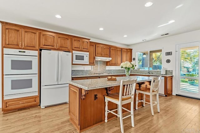 kitchen featuring white appliances, light hardwood / wood-style flooring, a kitchen breakfast bar, and a kitchen island