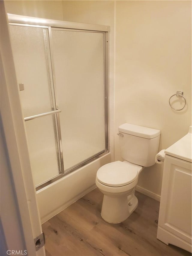 bathroom with bath / shower combo with glass door, hardwood / wood-style floors, and toilet