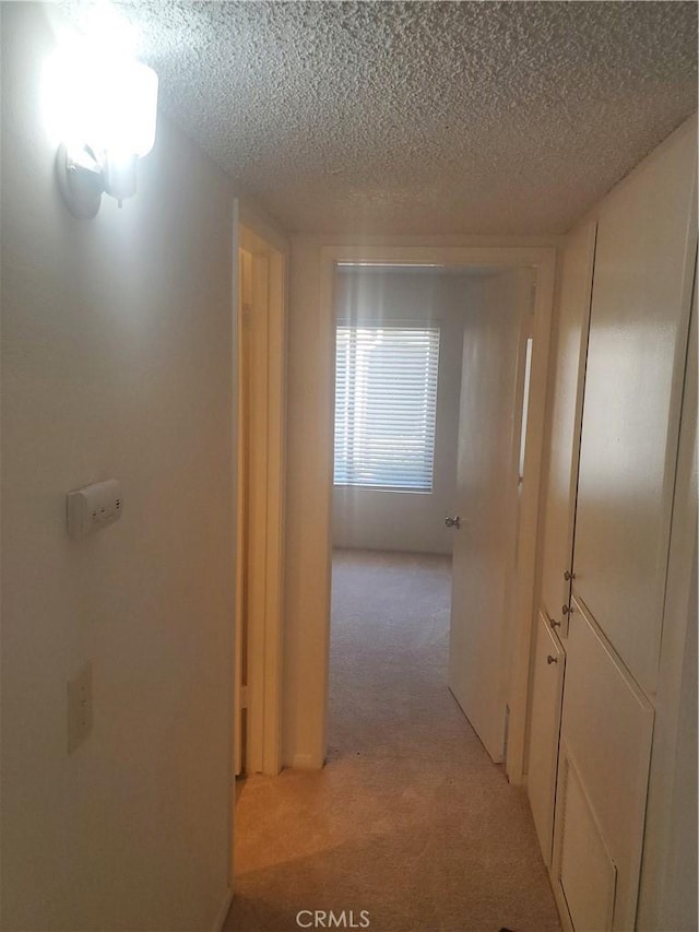 hallway featuring a textured ceiling and light colored carpet