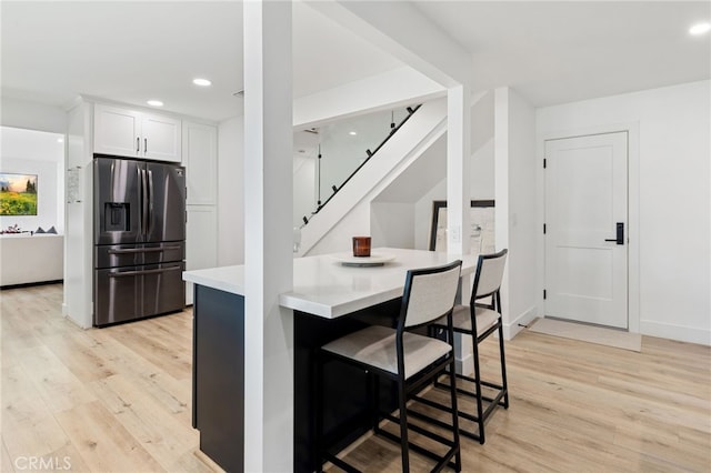 kitchen featuring light hardwood / wood-style floors, a kitchen breakfast bar, white cabinets, and stainless steel fridge with ice dispenser