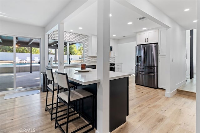 kitchen featuring stainless steel refrigerator with ice dispenser, white cabinetry, light hardwood / wood-style flooring, and a wealth of natural light