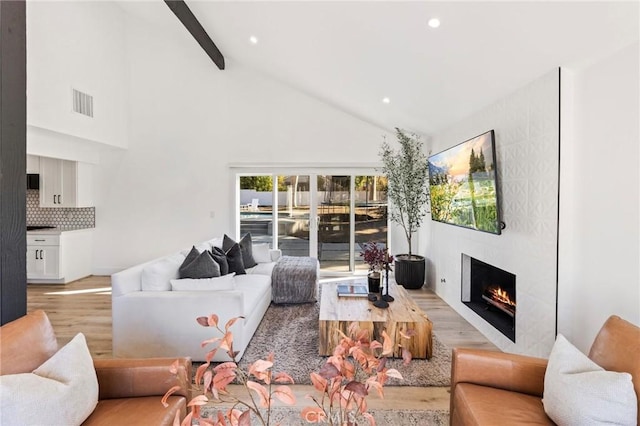 living room featuring high vaulted ceiling, light hardwood / wood-style floors, a large fireplace, and beamed ceiling