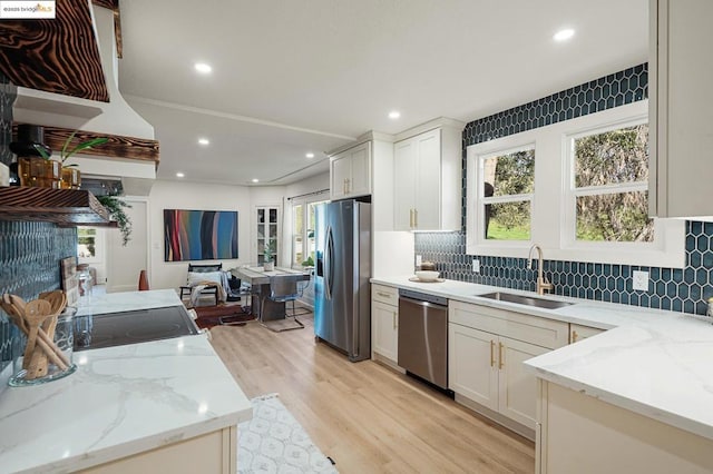 kitchen featuring appliances with stainless steel finishes, sink, white cabinets, light wood-type flooring, and light stone counters