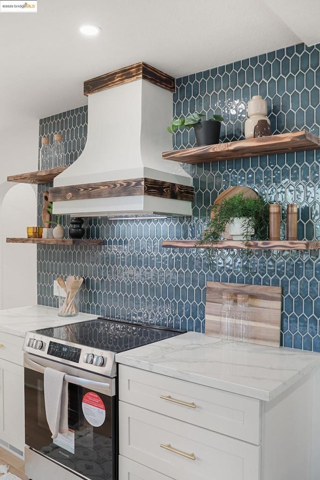 kitchen featuring premium range hood, white cabinetry, stainless steel electric range, backsplash, and light stone counters