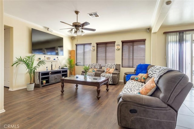 living area featuring dark wood finished floors, visible vents, ornamental molding, ceiling fan, and baseboards