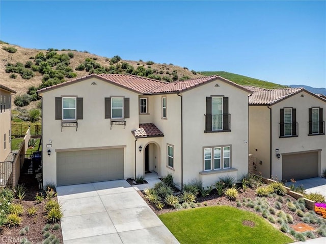 mediterranean / spanish-style home featuring concrete driveway, a tiled roof, an attached garage, and stucco siding