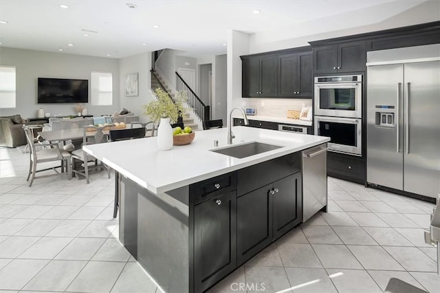 kitchen featuring sink, stainless steel appliances, an island with sink, and light tile patterned flooring