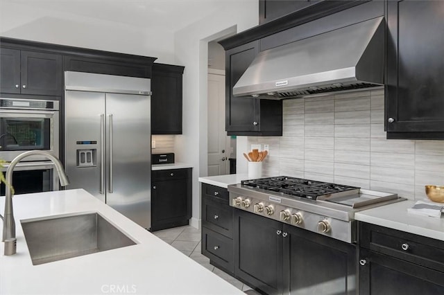 kitchen with appliances with stainless steel finishes, sink, backsplash, light tile patterned floors, and wall chimney exhaust hood